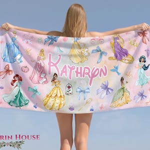 May include: A pink beach towel featuring illustrations of princesses, bows, and the name "Kathryn" in a cursive font. The towel has a light pink background with various princess designs and decorative elements.