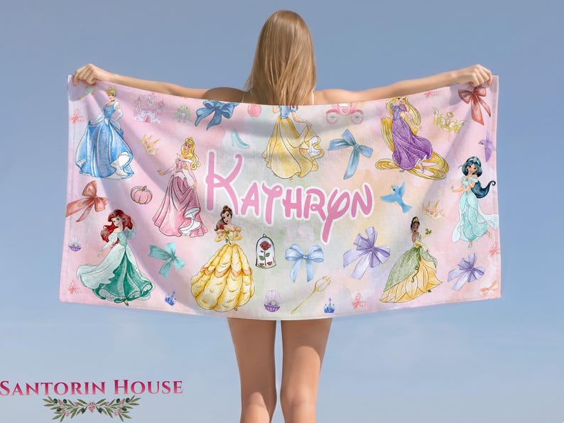 May include: A pink beach towel featuring illustrations of princesses, bows, and the name "Kathryn" in a cursive font. The towel has a light pink background with various princess designs and decorative elements.