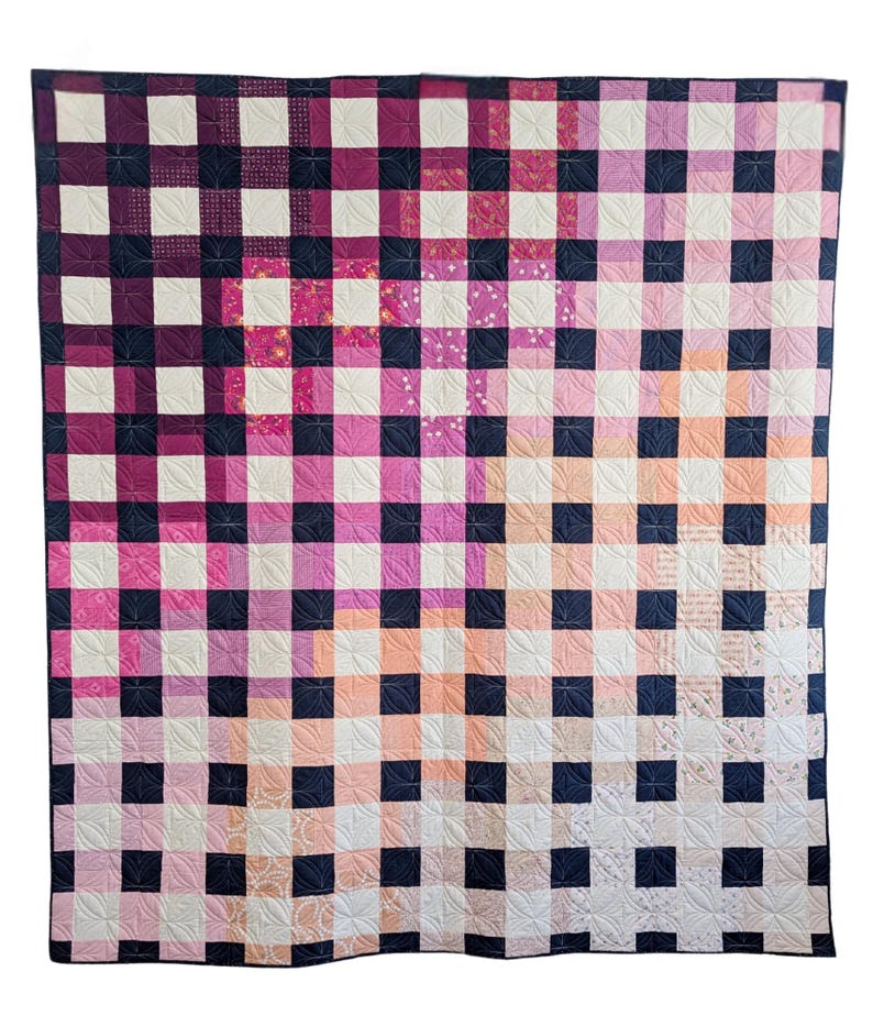 May include: A quilt with a checkered pattern in shades of pink, peach, and white. The squares are outlined in black.