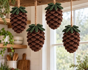 May include: Four crocheted pinecone ornaments hanging from a wooden beam by jute twine. Each ornament features a brown textured body with a dark green crocheted top. The pinecones are crafted with a repeating stitch pattern to mimic natural scales.