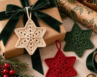 Pode incluir: Três ornamentos em forma de estrela de seis pontas feitos de crochê em fios nas cores creme, verde escuro e vermelho profundo. Cada estrela apresenta um motivo circular central com padrões vazados radiantes e uma alça de fio.