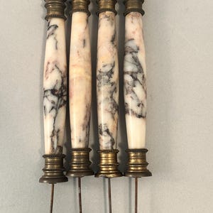 K&ouml;nnte beinhalten: Vier antike Marmorspie&szlig;e mit Messingakzenten. Die Spie&szlig;e haben ein wei&szlig;es und rosa Marmormuster mit dunkelgrauer Maserung. Jeder Spie&szlig; hat eine Ober- und Unterseite aus Messing und einen langen Metallstift.