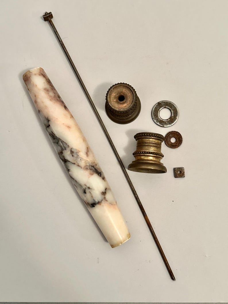 K&ouml;nnte beinhalten: Eine Ansammlung antiker Hardware-Komponenten, darunter ein Griff mit Marmormuster, Messingbeschl&auml;ge, Unterlegscheiben und eine Gewindestange. Der Griff ist wei&szlig; mit rosa und grauen Adern. Die Messingteile weisen Altersspuren auf.