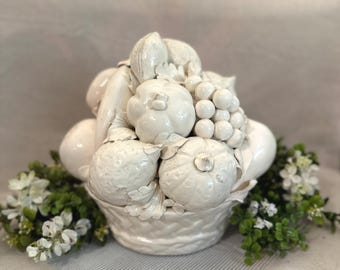May include: A white ceramic basket filled with a sculpted arrangement of various fruits including grapes, pumpkins, and citrus. The entire piece features a glossy, monochromatic white finish with detailed textures on each individual fruit.