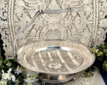 May include: A silver-toned metal basket with a high arched handle and a circular base supported by small feet. The interior of the bowl features an engraved pattern of vertical stripes and floral motifs, with a smooth, polished finish.