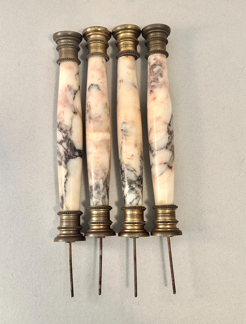 K&ouml;nnte beinhalten: Vier antike M&ouml;belgriffe aus Marmor und Messing. Die Griffe haben eine zylindrische Form mit einem Marmork&ouml;rper mit rosa und grauer Maserung. Ober- und Unterseite sind aus Messing mit einem dekorativen Design. Jeder Griff hat eine Metallstange, die sich von unten erstreckt.