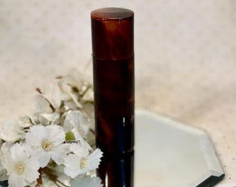 May include: A cylindrical container with a dark brown, mottled tortoiseshell pattern and a matching lid. The object stands upright, featuring a smooth, polished finish that reflects light across its surface, showcasing a rich, deep color palette.