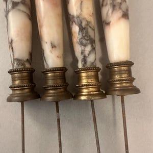 K&ouml;nnte beinhalten: Vier antike Spie&szlig;e aus Marmor und Messing. Die Marmorgriffe haben ein wei&szlig;es und graues Adernmuster. Die Messingbasen sind verziert, und die Spie&szlig;e haben lange, gewindef&ouml;rmige Metallst&auml;be.