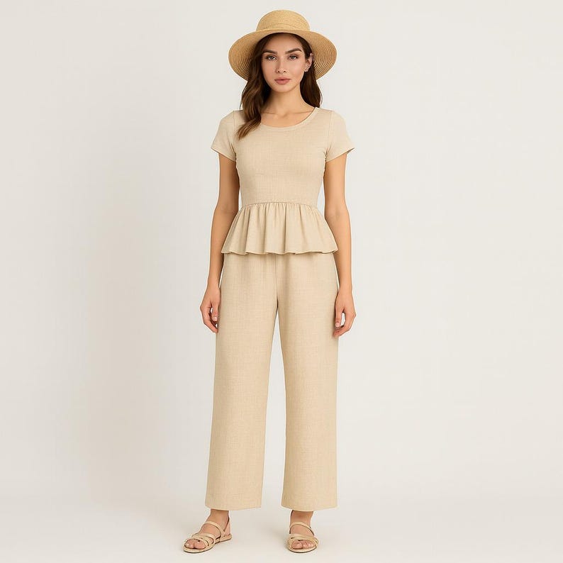 May include: A beige linen outfit comprising a short-sleeved top with a peplum waist and wide-leg trousers. The outfit is accessorized with a straw hat and sandals. The ensemble is a neutral colour, suitable for warm weather.