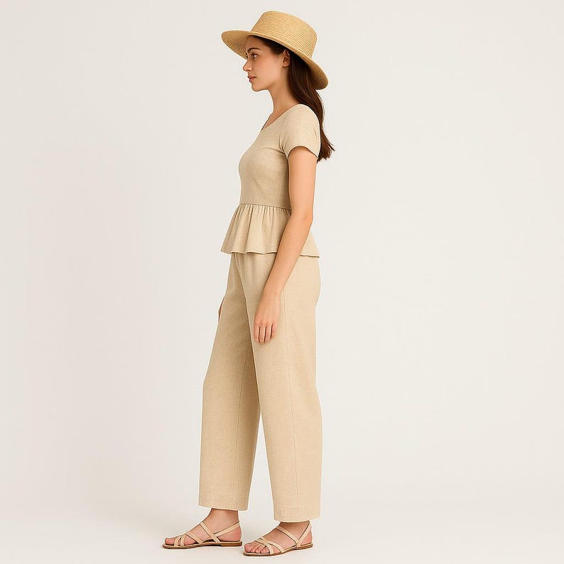 May include: A beige linen outfit comprising a short-sleeved top with a peplum, wide-leg trousers, a straw hat, and sandals. The outfit is a neutral colour and appears to be made of a lightweight fabric, suitable for warm weather.