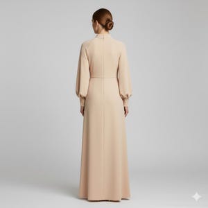 May include: A long, beige dress with a high neckline and long sleeves. The dress features a fitted bodice and a flowing skirt. The sleeves have a slight puff at the shoulder and are fitted at the wrist. The dress is made of a smooth, solid fabric.