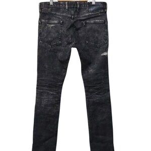 May include: Black denim jeans with a distressed, faded appearance. The jeans have a classic five-pocket design, a button and zipper closure, and are hanging on a wooden hanger. The jeans have a slim fit and are suitable for casual wear.