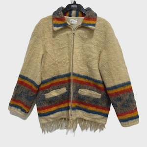 Puede incluir: Chaqueta de lana beige con cierre de cremallera completo, dos bolsillos delanteros y dobladillo con flecos. El cuello y las mangas tienen rayas horizontales azules, rojas, amarillas y marrones.