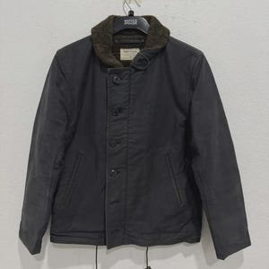 May include: A dark gray jacket with a brown fur-lined collar. The jacket has a button-up front, two front pockets, and drawstrings at the bottom. The Marks & Spencer label is visible on the collar.