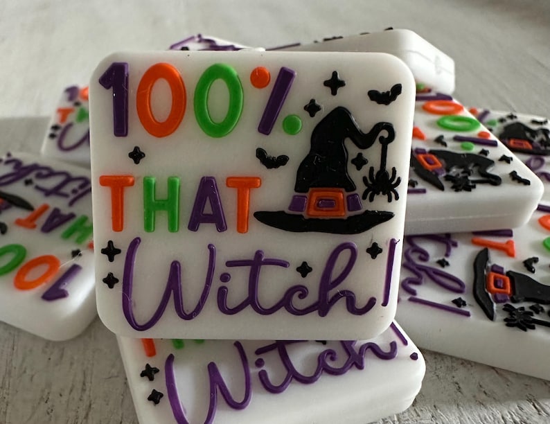 May include: White square soap bars with colorful Halloween-themed text and graphics. The bars feature the phrase "100% THAT Witch!" in orange, green, and purple. A witch hat and spider are also displayed.