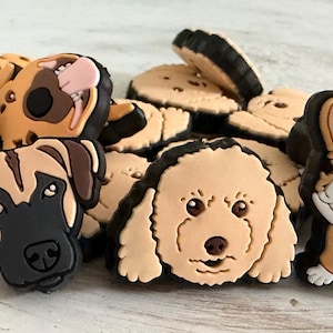 May include: A collection of colorful dog-themed charms. The charms feature various dog breeds, including a corgi, a poodle, and a German Shepherd. Each charm has a detailed, cartoon-like design with black outlines and vibrant colors.