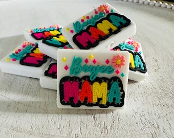 May include: White square-shaped decorative items with the word "Boyee MAMA" in colorful lettering. The letters are outlined in black and accented with small flowers and stars. The items are arranged on a white, textured surface.