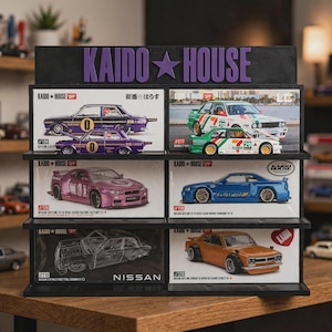 May include: A black three-tier display stand with the text KAIDO HOUSE in purple letters at the top. The stand holds six die-cast model cars in their individual boxes, featuring various Nissan Skyline and Datsun models in purple, green, pink, blue, and orange.
