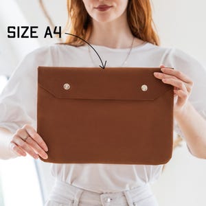 May include: A brown A4-sized laptop sleeve with two silver snap closures. The text "SIZE A4" is visible in the upper left corner. The sleeve is made of a smooth material and has a flap closure.