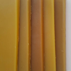 May include: Close-up of several rectangular bars of beeswax in varying shades of yellow and brown. The bars are arranged vertically, showcasing the natural color variations of the wax. The image highlights the texture and color of the beeswax.