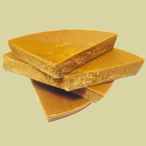 May include: Four pieces of golden-yellow beeswax are stacked, showcasing a natural, textured surface. The shapes are roughly triangular, with a slightly curved edge, suggesting they may be cut from a larger block. The color is consistent throughout, indicating a natural product.