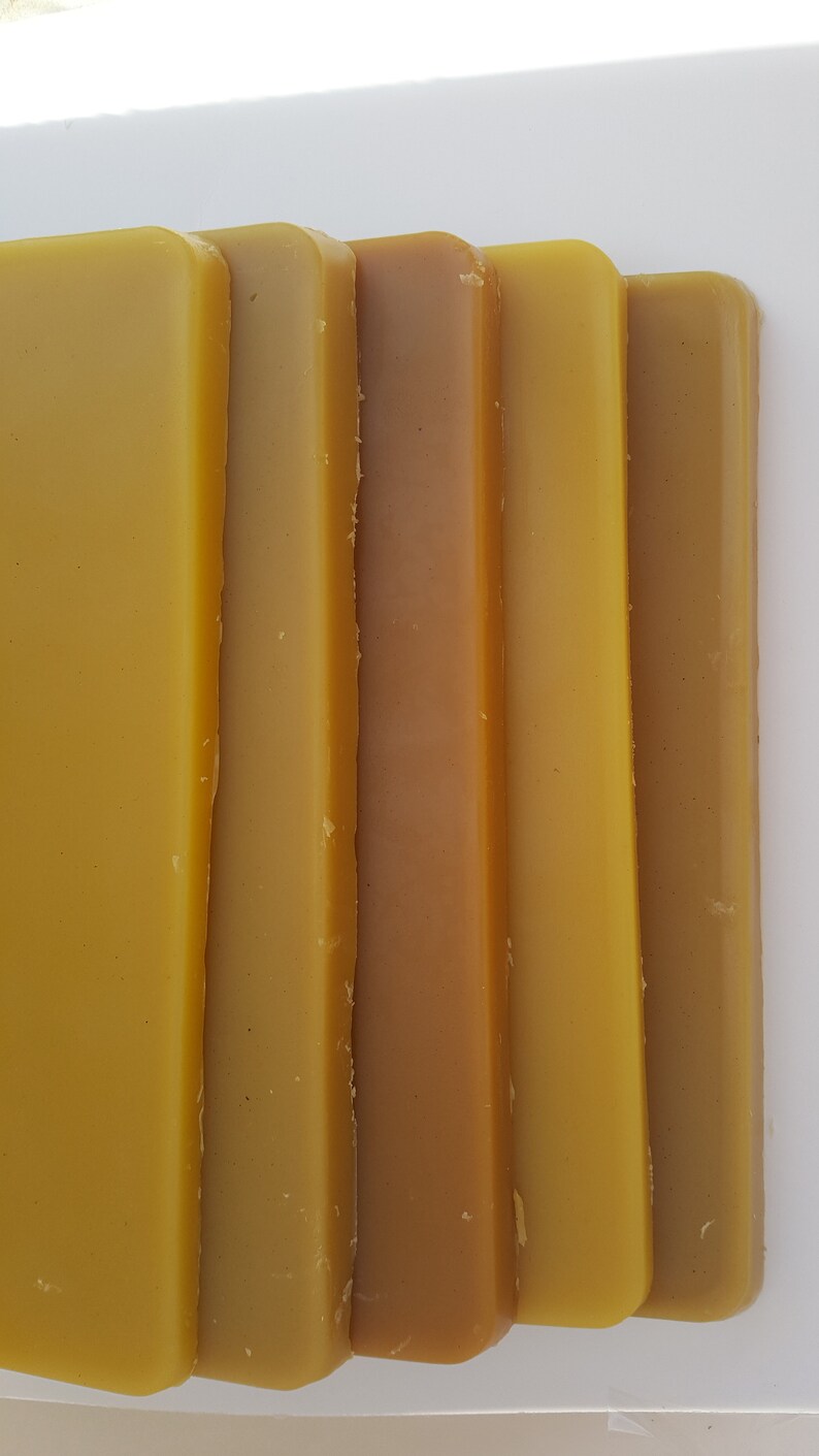 May include: Close-up of several rectangular bars of beeswax in varying shades of yellow and brown. The bars are arranged vertically, showcasing the natural color variations of the wax.