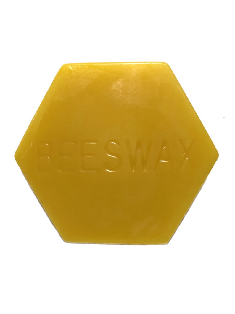 May include: A hexagonal block of yellow beeswax with the embossed word "BEESWAX". The wax has a smooth, slightly translucent appearance. The shape is a six-sided polygon, and the color is a warm, golden yellow.