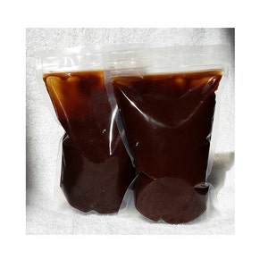 May include: Two clear plastic pouches filled with a dark brown liquid. The pouches are sealed at the top and appear to be sitting on a white surface. The liquid has a thick consistency.