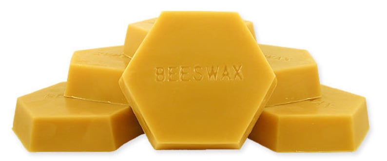 May include: Hexagonal blocks of yellow beeswax, stacked to show the product. The word "BEESWAX" is embossed on the central block. The blocks have a smooth, solid appearance, suggesting a natural product.
