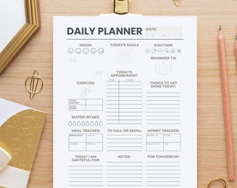 May include: A white daily planner sheet with a gold clip, pencils, and decorative items. The planner includes sections for mood, goals, appointments, exercise, water intake, meal tracker, and notes. The text "DAILY PLANNER" is at the top.