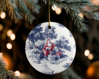 May include: Round Christmas ornament with a blue and white toile design featuring Santa Claus in a forest setting. Santa is wearing a red suit and is surrounded by gifts. The ornament hangs from a gold string.