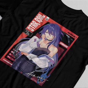 Op de afbeelding: Zwart T-shirt met een manga-stijl illustratie van een vrouw met paars haar en een witte jas. Het ontwerp bevat de tekst "STAR RAIL" en "ACHERON" in een rode rechthoek. Het shirt heeft ook Japanse tekst en de website "ELVENSHOPZ.COM".
