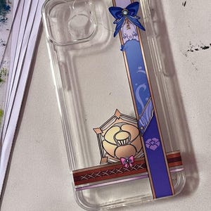May include: A clear flexible TPU phone case featuring a vertical purple band with a blue bow, a gold-toned geometric emblem, and a cross-stitched pattern. The text on the case reads: Flexible TPU Case | UV Print | Back Panel Only | Partial Design.