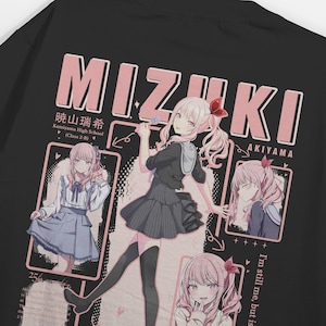 May include: Black t-shirt with a pink and white anime-style graphic of Mizuki Akiyama. The design includes Japanese text and illustrations of the character. The shirt also features the text "I'm still me, but is".