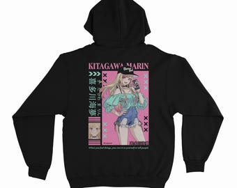 May include: A black hooded sweatshirt featuring a graphic print on the back. The design displays an anime-style character with blonde hair, a black cap, a teal off-shoulder top, and denim shorts, accompanied by Japanese text and the name KITAGAWA MARIN.