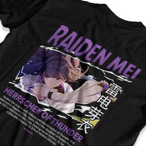 May include: Black t-shirt featuring a graphic of Raiden Mei, with the text "RAIDEN ME" in purple. Below the image, the text "HERRSCHER OF THUNDER" is displayed. Japanese characters are also present. The shirt is made of a soft material.
