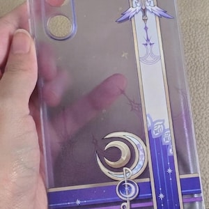 May include: A clear flexible silicone TPU phone case featuring a vertical purple and white graphic design with a central winged emblem and a crescent moon symbol. The case includes cutouts for a camera array and a semi-transparent print effect.