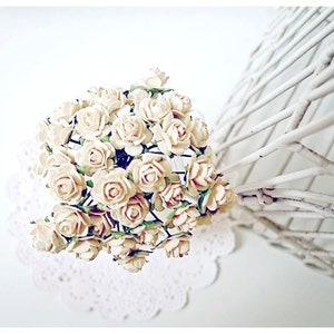 Op de afbeelding: Een boeket kleine, crèmekleurige papieren rozen met groene stelen, gerangschikt op een wit kantje.