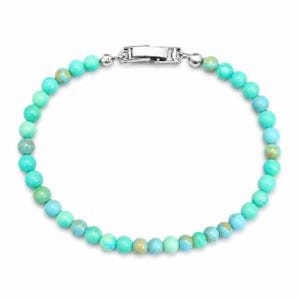 May include: A turquoise beaded bracelet with a silver clasp. The bracelet features small, round beads in shades of turquoise, blue, and green. The clasp is a simple, rectangular design. The bracelet is displayed on a white background.