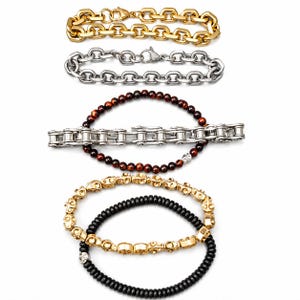 May include: An assortment of bracelets in various styles. The top bracelet is gold-toned with a chain link design. Below it is a silver-toned chain link bracelet. Other bracelets include beaded and chain designs in gold, silver, and black.