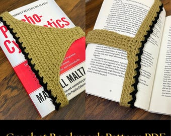 May include: A tan crochet bookmark with a black scalloped edge, shaped like a triangle with a strap, placed over an open book titled Psycho-Cybernetics by Maxwell Maltz. The text Crochet Bookmark Pattern PDF is displayed at the bottom.