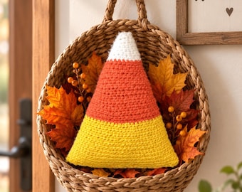 Può includere: Un peluche all'uncinetto a forma di caramella candy corn bianca, arancione e gialla, inserito in un cesto rotondo di vimini intrecciato. Il cesto è decorato con foglie d'acero autunnali artificiali nei toni del rosso, arancione e giallo.