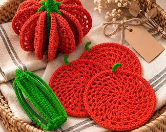 Può includere: Un set di oggetti all'uncinetto che include una zucca rossa con un gambo verde, una verdura cilindrica verde e tre sottobicchieri circolari rossi con piccoli gambi verdi, disposti su un tessuto chiaro all'interno di un cesto intrecciato.