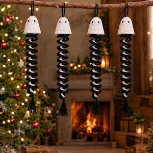 May include: Four hanging crochet ornaments, each featuring a white conical top with two small black eyes and a long, spiraling black and white striped body ending in a black yarn tassel. Each ornament is suspended by a black loop string.