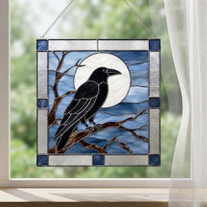 Op de afbeelding: Een vierkant glas-in-lood paneel met een zwarte raaf op een bruine boomtak tegen een grote witte volle maan en een blauwe lucht. Het werk is omlijst door een rand van getextureerd helder glas en kleine donkerblauwe vierkante glazen accenten.