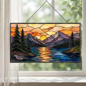 May include: A rectangular stained glass panel featuring a landscape scene with a sunset over mountains, a lake, and evergreen trees. The glass pieces are joined by dark metal lines, and the panel hangs from a thin black metal chain.