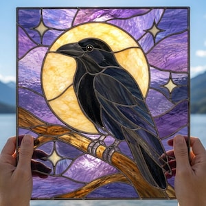 May include: A square stained glass panel featuring a black raven perched on a brown branch against a large yellow moon. The background consists of swirling purple glass segments accented with small, white, four-pointed star shapes.