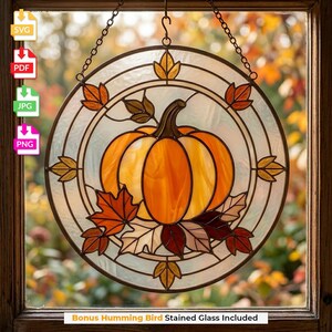 May include: A circular stained glass suncatcher featuring a central orange pumpkin surrounded by multi-colored autumn leaves in shades of red, brown, and gold. The design is encased in a round metal frame with a hanging chain and clear glass.