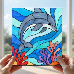 Könnte beinhalten: Ein quadratisches Buntglasfenster mit einem grauen Delfin, der durch stilisierte blaue und türkisfarbene Wellen springt. Der untere Bereich zeigt leuchtend rote, violette und orangefarbene Korallen vor einem tiefblauen Meeresgrund.