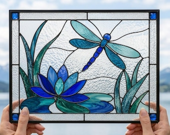 May include: A rectangular stained glass panel featuring a blue dragonfly hovering above a blue lotus flower and green lily pads. The design is framed in black metal with small blue glass accents in the corners and textured clear glass background.
